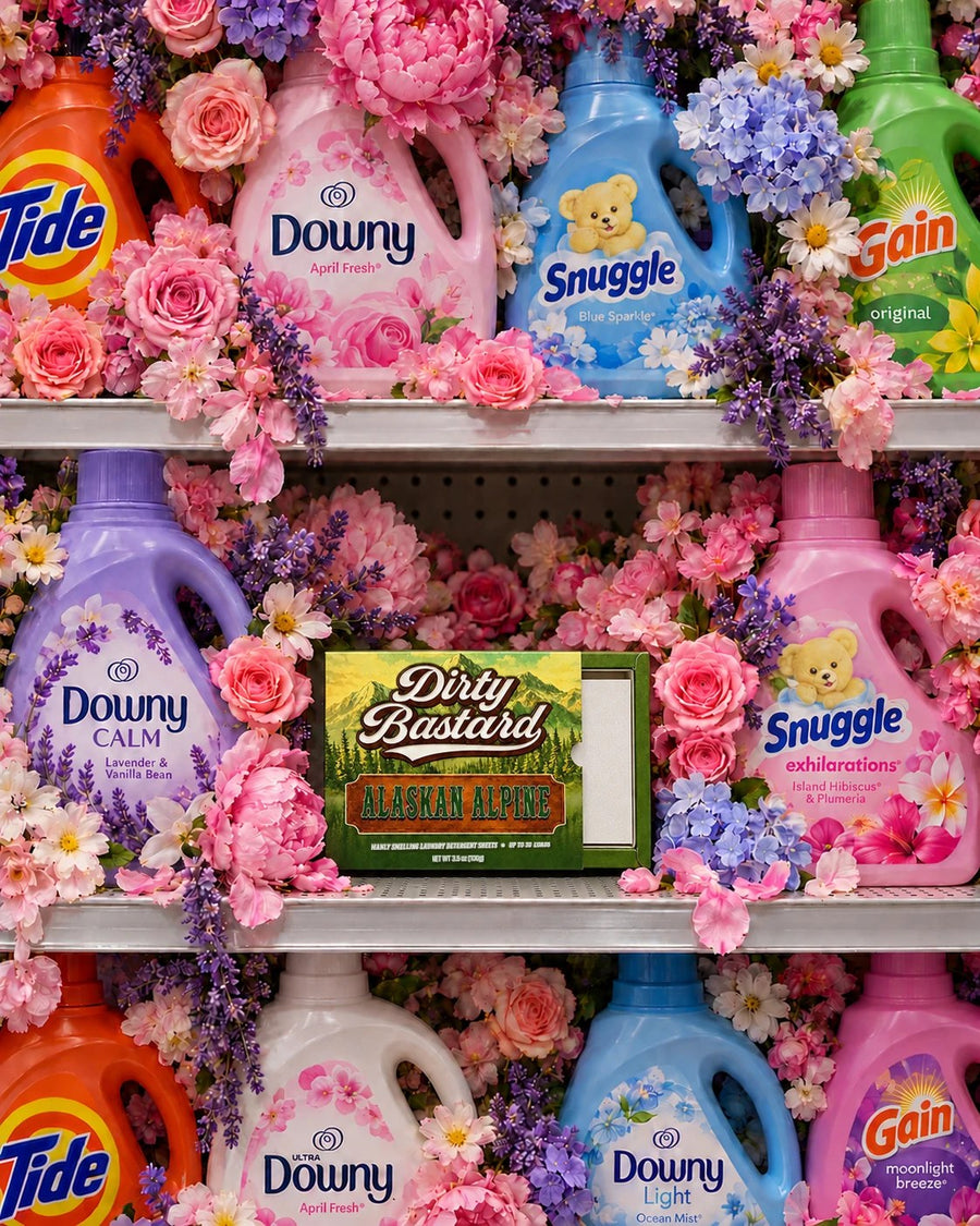 A box of Dirty Bastard Alaskan Alpine sits on a store shelf, surrounded by pink and lavender flowers and pastel floral detergent jugs.